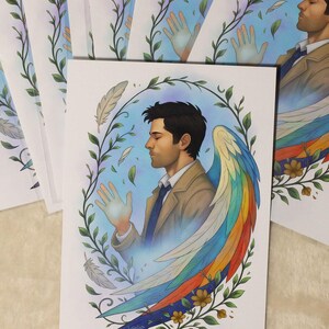 K&ouml;nnte beinhalten: Kunstdruck mit einem Mann mit Regenbogenfl&uuml;geln, umgeben von einem floralen Kranz und Federn. Das Bild hat eine weiche Farbpalette mit dem Text "The Quiet Radiance" unten. Mehrere Drucke sind gestapelt.