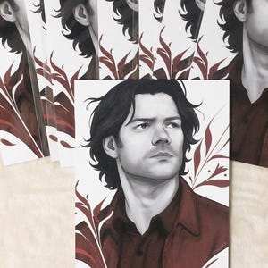 K&ouml;nnte beinhalten: Kunstdrucke mit einem Graustufenportr&auml;t eines Mannes mit dunklem Haar und einem weinroten Hemd. Die Drucke sind von weinroten floralen Akzenten umgeben. Der Text "Sam/Jared" befindet sich am unteren Rand des Bildes.