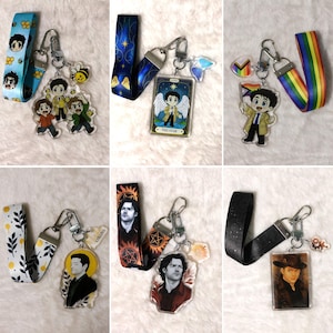 May include: Collection of lanyards and keychains featuring character art. The lanyards have various patterns, including stars, rainbows, and character faces. The keychains showcase characters in different poses and designs, with silver-tone hardware.