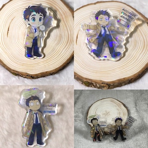 May include: Four clear acrylic charms featuring cartoon characters in a trench coat and suit. One holds a dandelion, another has arms outstretched, and two hold signs that read "Existential Crisis ACTIVATED" and "Socially Drained Angel".