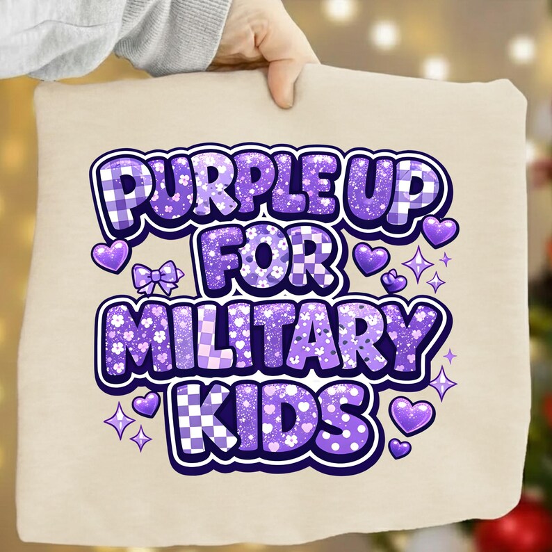May include: A beige pillow with the text "PURPLE UP FOR MILITARY KIDS" in purple. The text has a mix of patterns, including plaid and floral designs, with purple hearts, bows, and stars. The pillow is held by a person.
