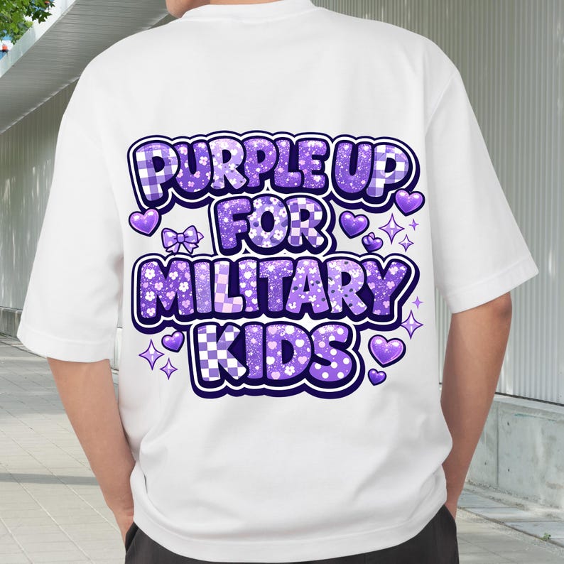 May include: White t-shirt with a large purple graphic that reads "PURPLE UP FOR MILITARY KIDS." The text is in a playful font with decorative hearts, bows, and stars. The design incorporates checkered and floral patterns.