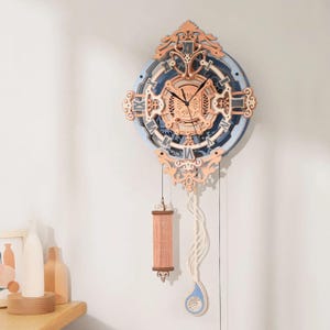 May include: A decorative wooden wall clock with a blue, brown, and white color scheme. The clock features Roman numerals, intricate cut-out designs, and a pendulum. The clock is hanging on a white wall.