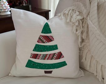 Könnte beinhalten: Ein weißes Kissen mit einem grünen Weihnachtsbaumdesign. Der Baum besteht aus Stoffresten mit roten und weißen Mustern.