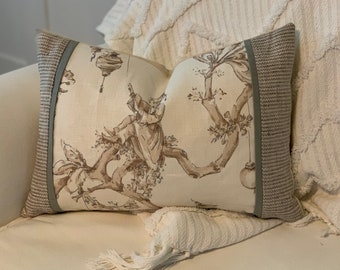 May include: A decorative throw pillow with a beige linen fabric and a brown and green floral pattern. The pillow has a light green trim around the edges.