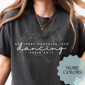 May include: Dark gray t-shirt with the text "He turns mourning into dancing" and Psalm 30:11. The shirt features a line drawing of dancers. A teal sticker says "More Colors".