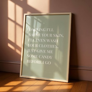 Puede incluir: Una impresión artística enmarcada con un fondo verde salvia y un marco dorado. El texto blanco dice: "DARLING I'LL BATHE YOUR SKIN, I'LL EVEN WASH YOUR CLOTHES, JUST GIVE ME SOME CANDY BEFORE I GO."