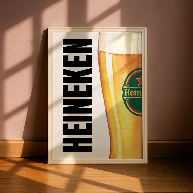 Puede incluir: Impresi&oacute;n enmarcada con una ilustraci&oacute;n de un vaso de cerveza lleno de cerveza dorada. La palabra "HEINEKEN" est&aacute; impresa verticalmente en letras negras en negrita en el lado izquierdo. El logotipo de Heineken es visible.