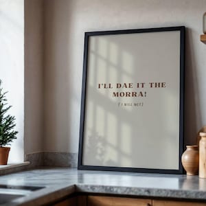 Könnte beinhalten: Ein gerahmter Druck mit dem Text "I'LL DAE IT THE MORRA! (I WILL NOT)" in braunen Buchstaben. Der schwarz gerahmte Druck lehnt an einer Wand auf einer Küchenarbeitsplatte. Ein kleiner Topf-Immergrünbaum steht auf der Fensterbank.
