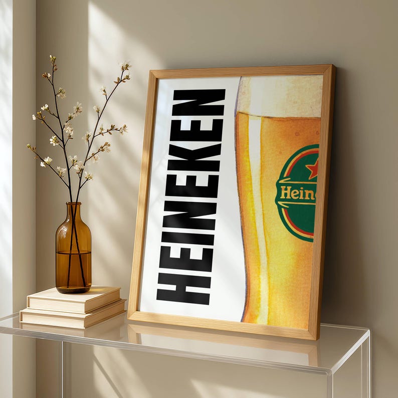 Puede incluir: Un cartel enmarcado con el logotipo de Heineken y una imagen parcial de un vaso de cerveza. La palabra "HEINEKEN" est&aacute; impresa verticalmente en letras negras en negrita. El vaso de cerveza tiene espuma y un logotipo verde y rojo.