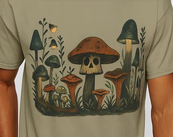 May include: Olive green t-shirt featuring a detailed illustration of various mushrooms in shades of brown, orange, and green. The design includes a mushroom with a skull-like face. The shirt is made of a soft material.