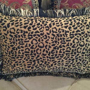 May include: A brown and black leopard print throw pillow with a black and white fringe trim.