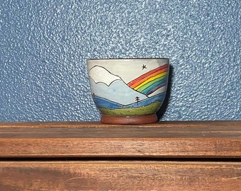 Bowl, rainbow over mountain and forest.