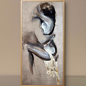 May include: Abstract painting in a gold frame. The artwork features a figure rendered in shades of gray, white, and black, with a textured gold leaf accent at the bottom. The background is a neutral beige.
