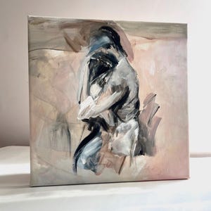 May include: A square canvas painting featuring an abstract human figure rendered in expressive brushstrokes of black, white, gray, and muted pink. The central form is depicted in a seated, hunched posture against a soft, blended background.