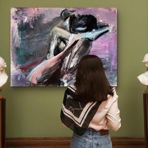 May include: An abstract painting of a couple embracing, in black, grey, pink, and purple hues. The artwork is displayed on a green wall, viewed by a person wearing a white shirt, blue jeans, and a black and white scarf.