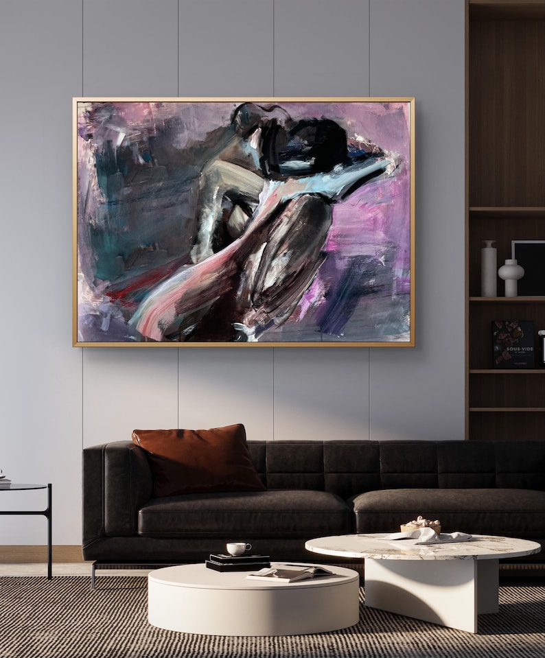 May include: Abstract artwork in a gold frame, depicting figures in black, grey, pink, and purple hues. The painting hangs above a black sofa with a brown cushion, a white coffee table, and a dark rug in a living room setting.