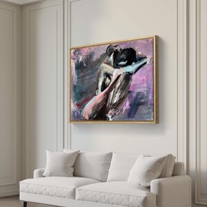 May include: Abstract artwork depicting a seated figure in purple, black, and pink hues. The painting, in a gold-toned frame, hangs above a white sofa with cushions. The artwork's style is modern and expressive, suitable for contemporary interiors. The painting is in a gold-toned frame.