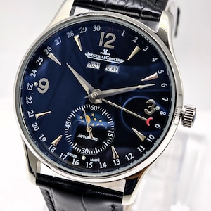 May include: A silver-tone automatic wristwatch with a dark blue dial, featuring a black leather strap, a moon phase sub-dial, and a calendar display showing 2031 and MAY. The dial includes the text Jaeger-LeCoultre, AUTOMATIC, and SWISS MADE.