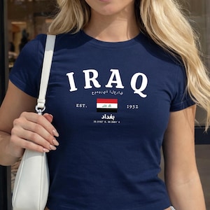 May include: Navy blue t-shirt with the word "IRAQ" in white block letters. Below the word "IRAQ" is the text "EST. 1932" and the Iraqi flag. The shirt also has Arabic text and the word "Baghdad".