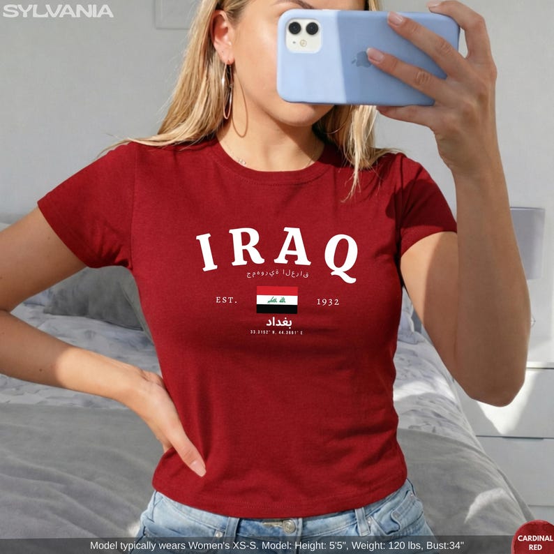 May include: Cardinal red t-shirt with the word "IRAQ" in white block letters. Below the word "IRAQ" is text in Arabic, the Iraqi flag, and the word "Baghdad". The shirt also has the text "EST. 1932".