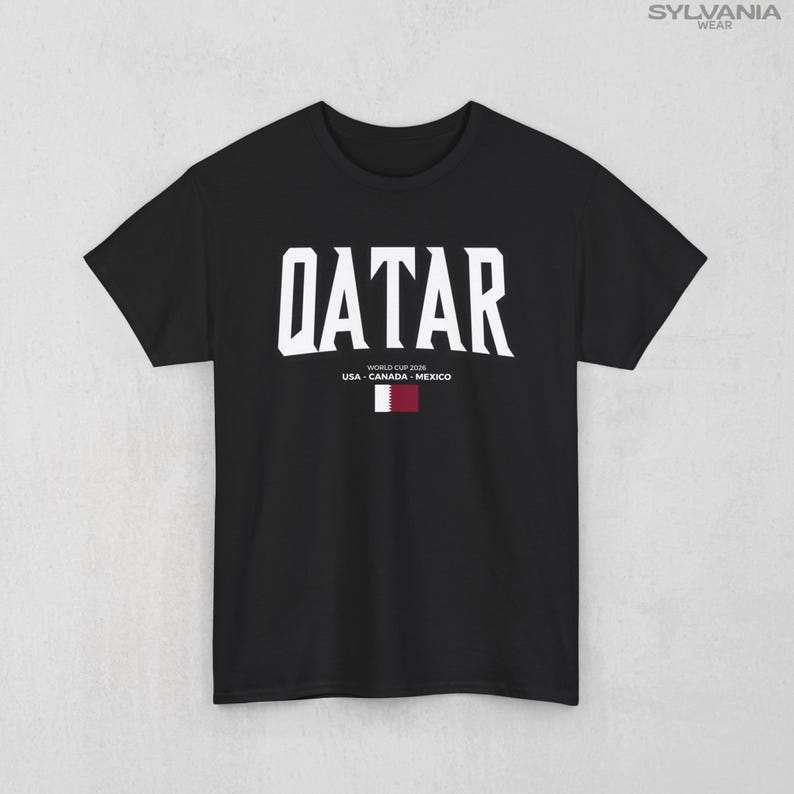 May include: Black t-shirt with the word "QATAR" in large white block letters. Below the word are the words "WORLD CUP 2026" and "USA - CANADA - MEXICO" in smaller white letters. A small flag of Qatar is below the text.