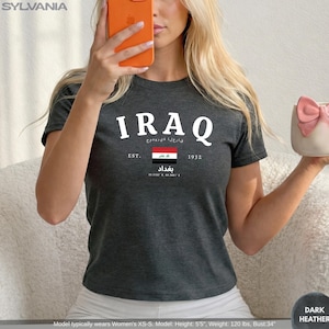 May include: Dark heather gray t-shirt with the word "IRAQ" in white block letters. Below the word "IRAQ" is text in a different language, the Iraqi flag, and the word "Baghdad". The shirt also has the text "EST. 1932".