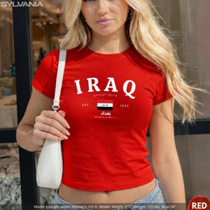 May include: A red crop top with the word "IRAQ" in white block letters. Below the word "IRAQ" is text in Arabic, the Iraqi flag, and the word "Baghdad". The shirt also has the text "EST. 1932".