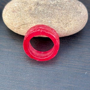 Peut inclure: Une bague rouge vif avec des détails floraux sculptés. La bague est une bande pleine, présentant une couleur audacieuse et un design complexe. C'est un accessoire de mode.