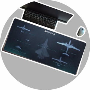 May include: A rectangular black mousepad featuring several aircraft silhouettes and the text "BAYKAR". A keyboard and mouse are visible above the mousepad. The mousepad has a dark background with white aircraft outlines.