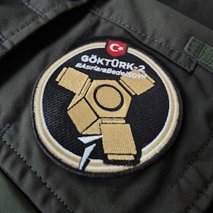 May include: A white ceramic mug with a black handle and the text "But First, Coffee" in a bold, black font. The mug is set against a blurred background, suggesting a cosy setting.