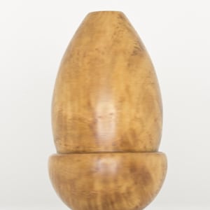 May include: A smooth, light brown wooden vessel with a rounded base and a tapered, egg-shaped top section. The object features a visible natural wood grain pattern with darker swirls throughout the surface, creating a polished and uniform appearance.
