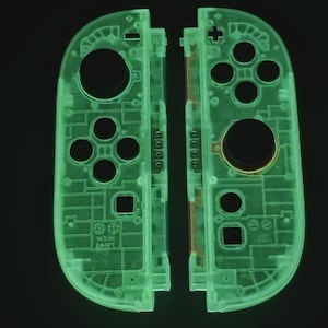 May include: Two neon green Nintendo Switch Joy-Con controllers, displayed side-by-side against a black background. The controllers are transparent, revealing internal components. Each controller has buttons, a joystick, and a circular hole.