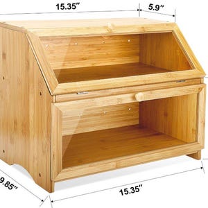 May include: A bamboo bread box with a clear glass door and a hinged top. The box is 15.35 inches wide, 12.6 inches tall, and 5.9 inches deep. The bottom compartment is 7.87 inches tall. The bread box has a natural wood finish.