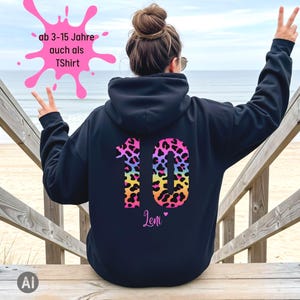 Könnte beinhalten: Ein schwarzer Kapuzenpullover mit der großen Zahl 10 auf dem Rücken, die ein buntes Leopardenmuster in Pink, Gelb und Blau aufweist. Unter der Zahl steht der Name Leni in einer Schreibschrift, ergänzt durch ein kleines pinkes Herz.