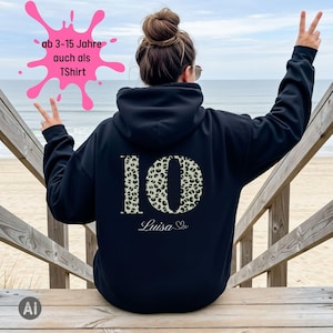 Könnte beinhalten: Ein schwarzer Kapuzenpullover mit einer großen Zahl 10 im Leopardenmuster auf der Rückseite. Unter der Zahl steht der Name Luisa in weißer Schreibschrift. Eine pinke Grafik enthält den Text ab 3-15 Jahre auch als TShirt.
