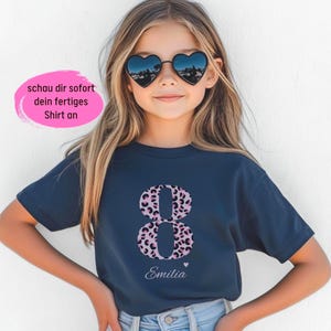 Könnte beinhalten: Ein dunkelblaues T-Shirt mit kurzen Ärmeln und einer großen Acht mit pinkfarbenem und schwarzem Leopardenmuster. Unter der Zahl steht der Name Emilia in weißer Schreibschrift mit einem kleinen Herz. Ein pinkfarbenes Oval enthält den Text schau dir sofort dein fertiges Shirt an.