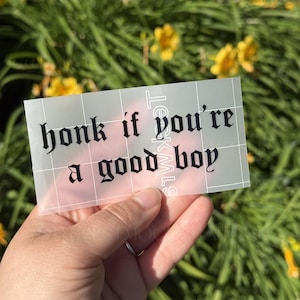 May include: A rectangular adhesive decal featuring the black text "honk if you're a good boy" in a gothic-style font. The sticker is printed on a semi-transparent transfer sheet with a white grid pattern overlaying the surface of the decal.