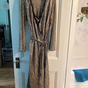 May include: A long-sleeved wrap robe featuring a brown and black leopard print pattern. The garment includes a V-neckline trimmed with black lace, long sleeves with ruffled cuffs, and a matching fabric tie belt at the waist for closure.