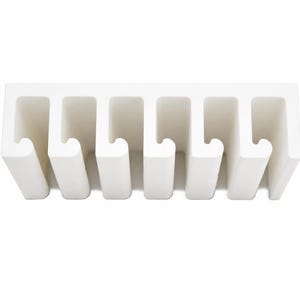 May include: A white wall-mounted organizer featuring six evenly spaced vertical slots with curved hook-like ends. The structure is rectangular with a solid top bar and uniform open channels designed for holding items in a linear arrangement.
