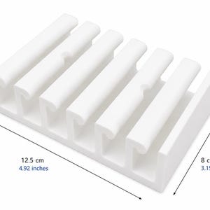 May include: A white rectangular cable organizer with five parallel slots for cord management. The unit measures 4.92 inches in length, 3.15 inches in width, and 1.26 inches in height, featuring a structured design to hold multiple cables securely in place.
