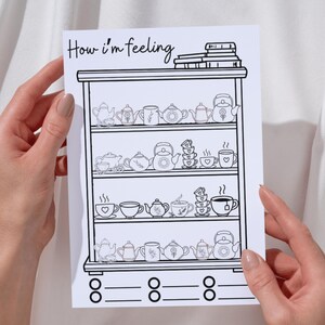 Può includere: Illustrazione in bianco e nero di una mensola piena di teiere, tazze e piattini. Il testo "How I'm feeling" è in alto. L'immagine è tenuta da due mani.