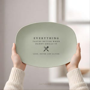 May include: A light green oval serving platter with black text that reads "EVERYTHING TASTES BETTER WHEN DADDY GRILLS IT" and "LOVE, BRYNN AND OLIVER". The platter has a crossed fork and spatula graphic.