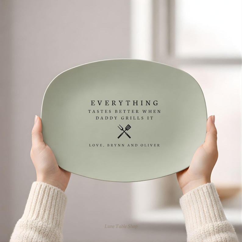 May include: A light green oval serving platter with black text that reads "EVERYTHING TASTES BETTER WHEN DADDY GRILLS IT" and "LOVE, BRYNN AND OLIVER". The platter has a crossed fork and spatula graphic.