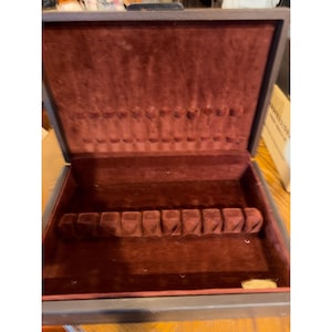 May include: A dark gray rectangular storage case with a hinged lid, featuring a deep burgundy velvet interior lining. The interior includes a molded velvet insert with ten individual slots for organizing items, plus additional storage space.
