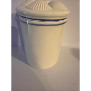 May include: A white ceramic jar with a lid featuring seashell designs. The jar has a cylindrical shape with a blue stripe near the top. The lid is adorned with three seashell shapes.