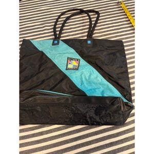May include: A black tote bag with a diagonal turquoise stripe and two black handles. A square patch features the text GITANO with a geometric pattern. A yellow measuring tape is visible in the corner, showing a length of approximately 3 inches.