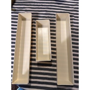 May include: Three rectangular, off-white plastic storage trays of varying lengths. Two long, narrow trays are positioned on the left and right, while a shorter, smaller tray is centered between them. Each tray features smooth, solid walls.