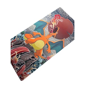 May include: A rectangular mousepad featuring a vibrant illustration of Charizard, an orange and yellow dragon-like creature, breathing fire. The background includes a red sun, blue floral patterns, and gray clouds.