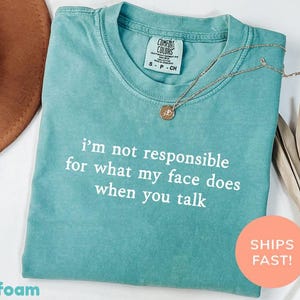 Könnte beinhalten: Türkisgrünes T-Shirt mit dem weißen Text "I'm not responsible for what my face does when you talk". Eine goldene Halskette mit Anhänger liegt auf dem Shirt. Das Shirt ist gefaltet und hat ein Comfort Colors-Etikett.